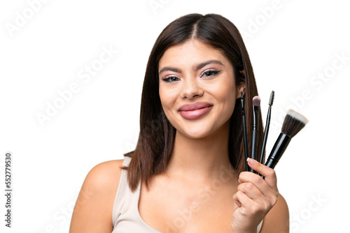 Young Russian woman with rainproof coat and umbrella over isolated chroma key background holding makeup brush