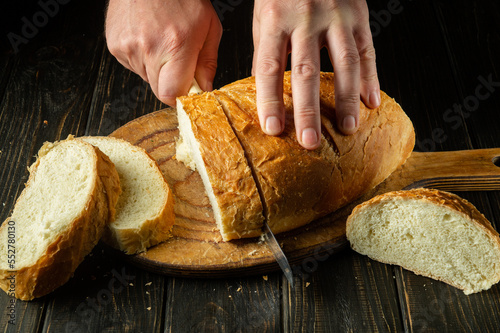 Whole grain bread put on kitchen wood board with a chef holding knife for cut. Fresh bread on table close-up. Wheat bread on the kitchen table or the healthy eating and traditional bakery concept