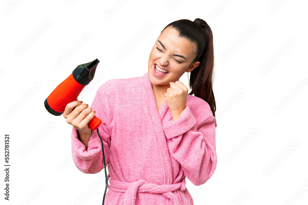 Young woman in a bathrobe holding a hairdryer over isolated chroma key background celebrating a victory Young woman in a bathrobe holding a hairdryer over isolated chroma key background celebrating a victory