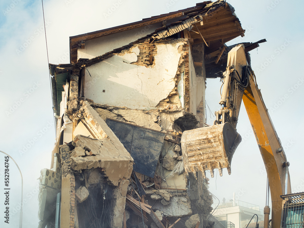 Fototapeta premium Process of demolition of civil building dismantling. Excavator breaking walls. renovation of the housing stock