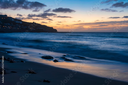 Stunning landscape image of Sennen Cove in Cornwall during sunset with dramatic sky and long exposure sea motion