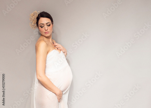 splendida donna incinta in abito bianco che guarda dolcemente verso il basso tenendosi la pancia con spazio libero per testo