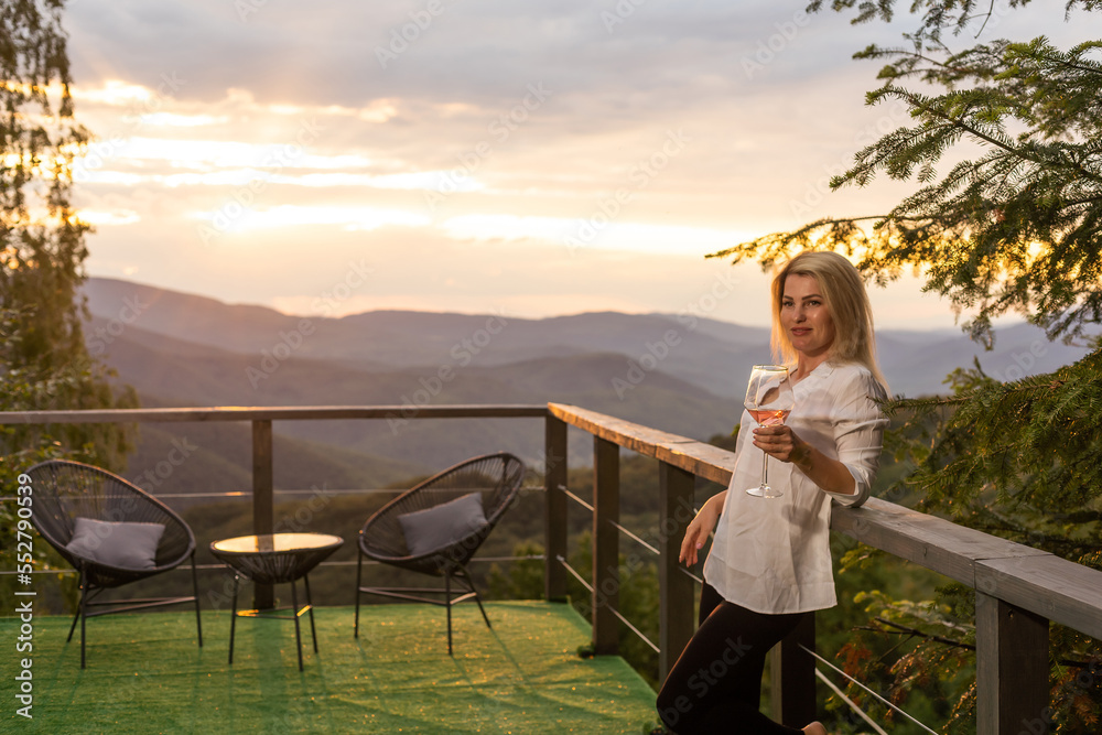 Woman holding glass of white wine across beautiful mountains landscape and sunset