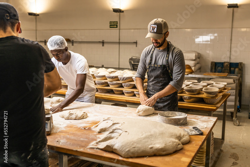 Caucasian master baker teaching the kneading technique to his African apprentice in the bread factory.