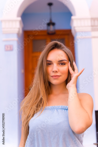 Portrait of attractive young blonde woman in blue dungarees smiling at the front door of her blue house