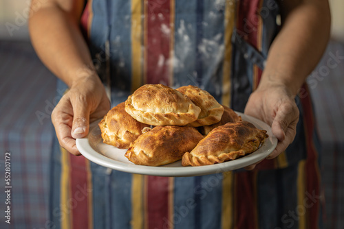 Fototapeta Naklejka Na Ścianę i Meble -  Woman in an apron stained with flour holding a tray with Argentine empanadas.