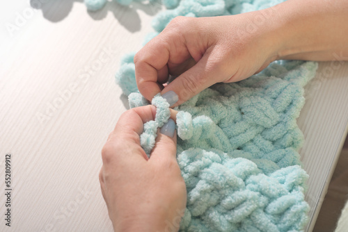 woman knitting with fingers turquoise plaid. Finger Knit a Chunky Yarn Blanket. hands of knitting woman. copy space. photo