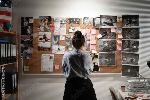 Young female detective looking at evidence board, back view. photo