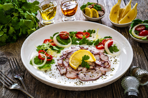 Octopus carpaccio with lemon and greens on wooden table 