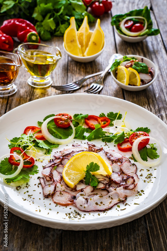 Octopus carpaccio with lemon and greens on wooden table 