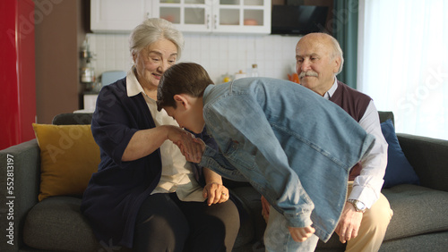 The little boy visited his grandfather and celebrated Eid al-Fitr by kissing their hands. Happy senior couple sitting on sofa kissing and hugging their little grandchild. 