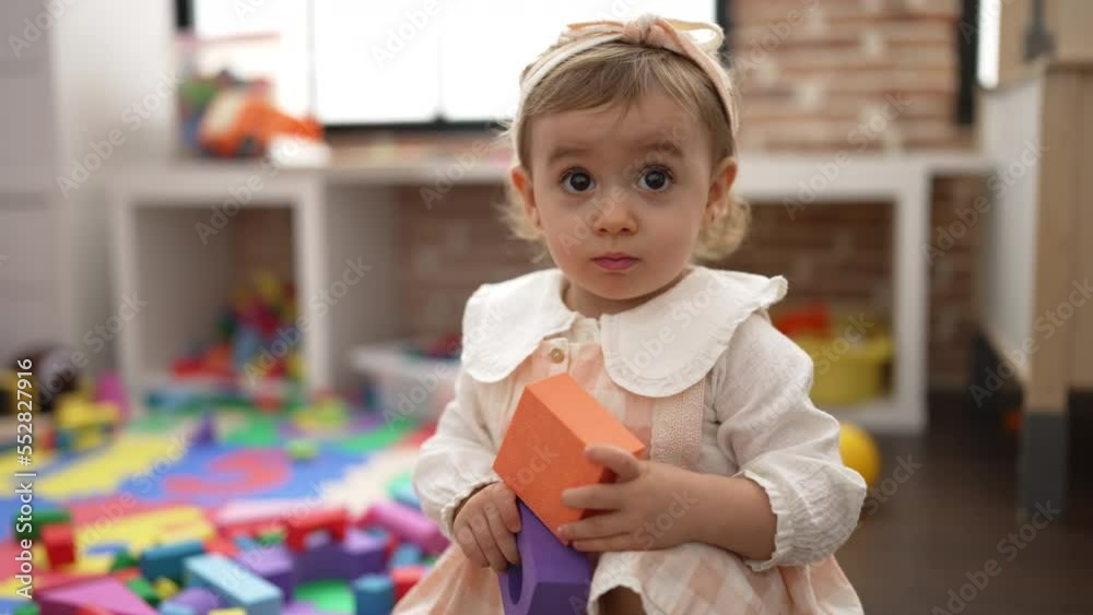 Adorable caucasian girl holding toy sitting on floor at kindergarten Adorable caucasian girl holding toy sitting on floor at kindergarten