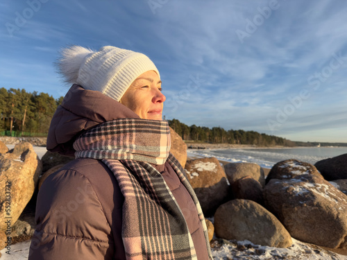 Portrait of beautiful happy senior retired elderly woman is enjoying good cold frosty sunny day at winter snow park with eyes closed, breathing deeply deep fresh air smiling at snowy beach, ocean
