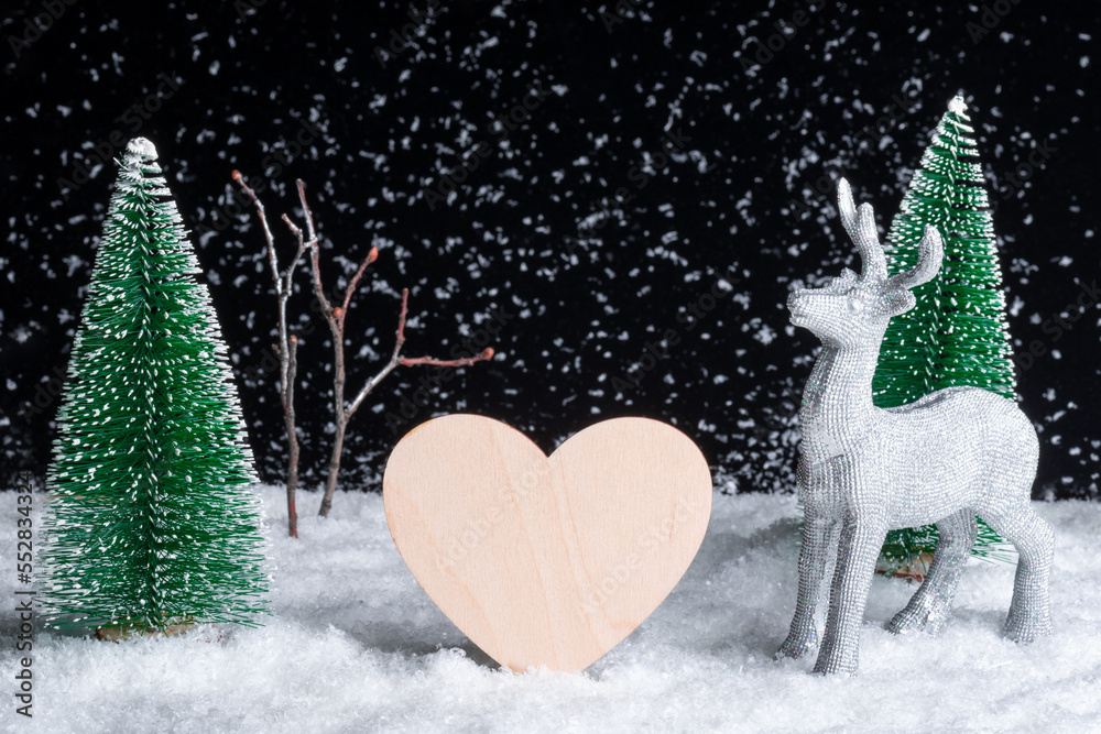 Creative Christmas card. Craft from toy trees in a snowfall at night, a wooden heart and a Christmas deer