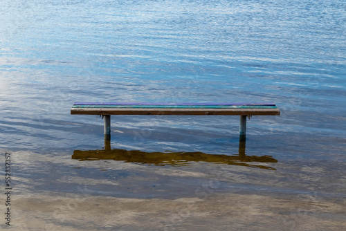 A wooden bench stands in the water during the day close-up
