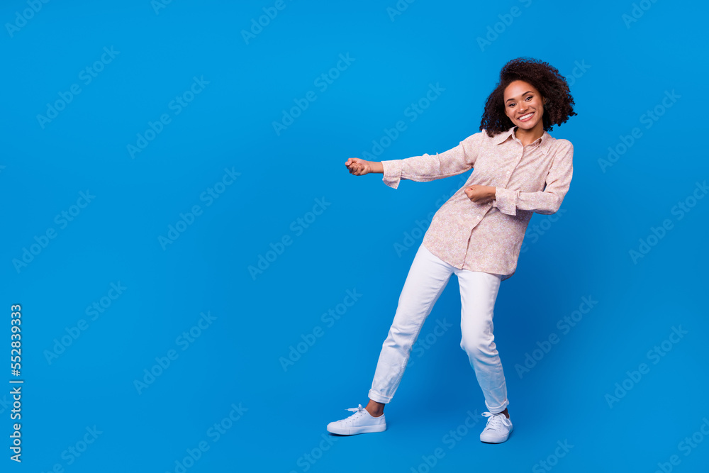 Full length photo of adorable funky girl dressed pink blouse pulling empty space isolated blue color background Full length photo of adorable funky girl dressed pink blouse pulling empty space isolated blue color background