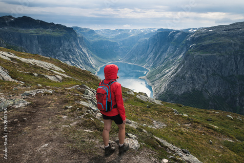 Young tourist woman in red jacket watching the view on the beautiful Ringedalsvatnet Lake. Hiking in Norwegian nature in windy weather. 