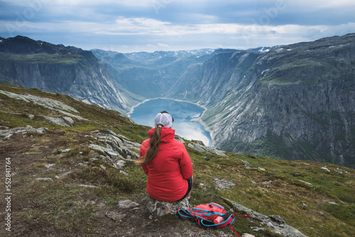 Young tourist woman in red jacket watching the view on the beautiful Ringedalsvatnet Lake. Hiking in Norwegian nature in windy weather. 