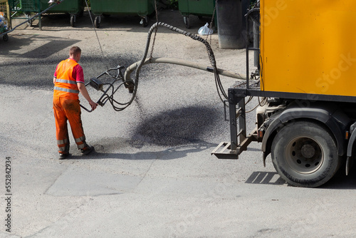 An employee of the road service fills the hole in the road surface with emulsion with rubble with a special machine for pit repair. 
