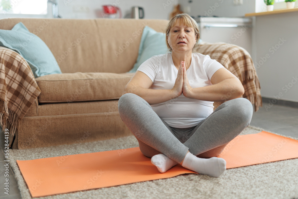 Mature woman doing yoga on fitness mat at home in the living room