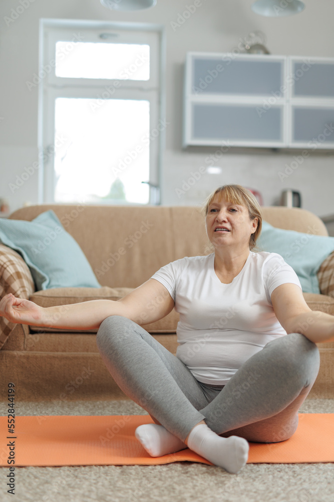 Mature woman doing yoga on fitness mat at home in the living room