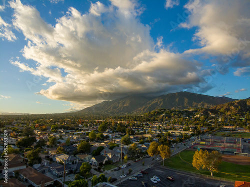 aerial shot of majestic mountains with powerful clouds and blue sky with homes, apartments and lush green trees in Monrovia California USA photo