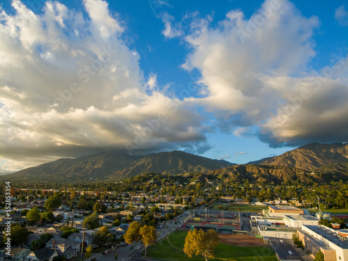 aerial shot of majestic mountains with powerful clouds and blue sky with homes, apartments and lush green trees in Monrovia California USA photo