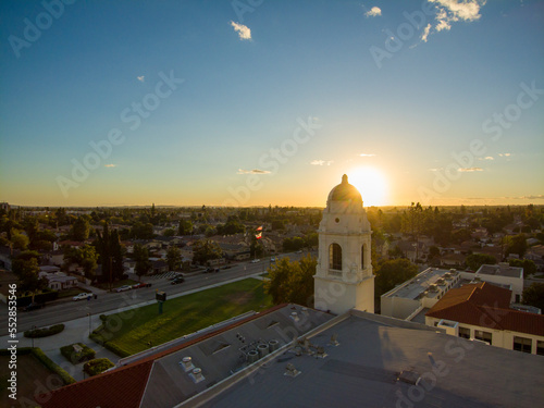 aerial shot of homes, apartments, and shops in the city skyline with cars driving on the street lush green trees and the bell tower at Monrovia High School at sunset in Monrovia California USA photo