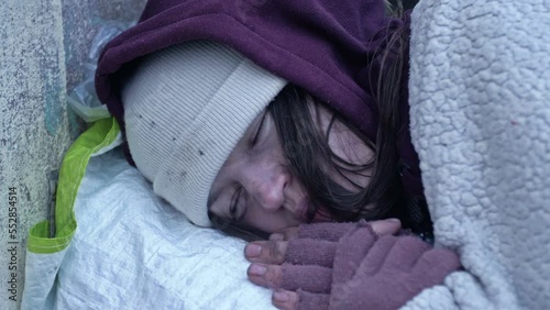 Young homeless woman sleeps on the street. Poorly and dirtily dressed, she freezes as she lies on the cold ground.