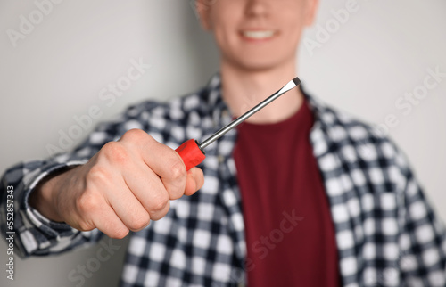 Handyman with screwdriver against light background, focus on hand © New Africa