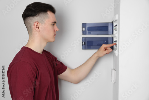 Young handyman pressing switch on electrical panel board indoors