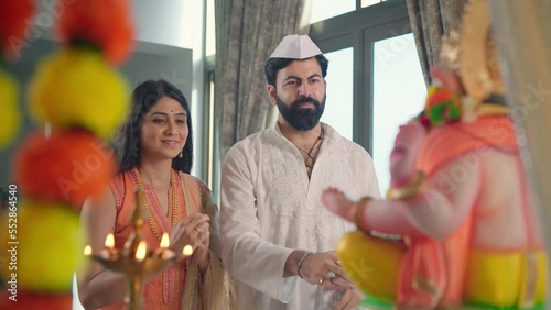 Happy ethnic Hindu Indian married couple in traditional clothes offering a prayer to a god called aarti with a Namaste posture and Marigold flowers in an indoor home. Religion, devotion, faith concept