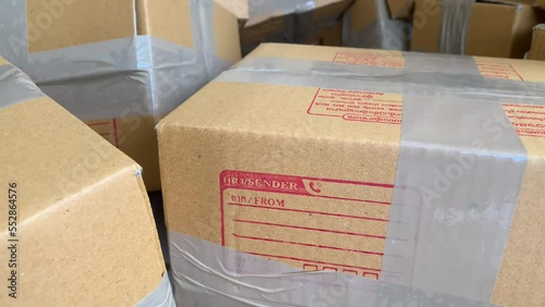 Close up cardboard box package with sender and postcode word screen on parcel with pile of wrapped boxes 