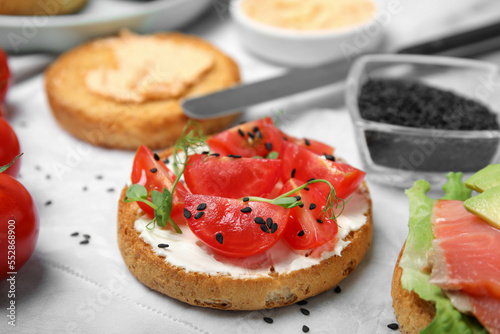 Tasty rusk with cream cheese, fresh tomatoes and black sesame seeds on white table, closeup