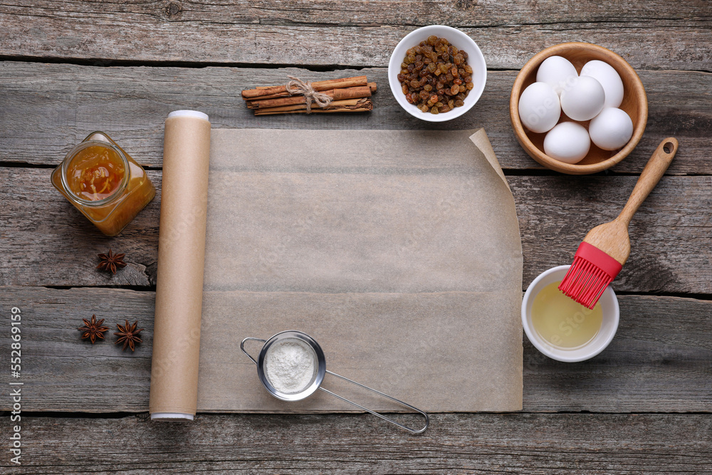 Roll of baking parchment paper, different ingredients and kitchen tools on wooden table, flat lay. Space for text