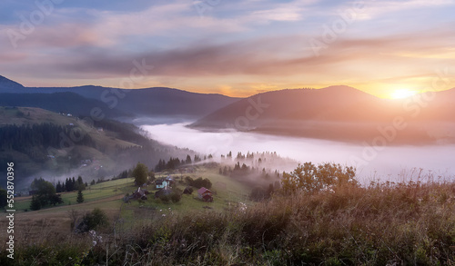 Beautiful vivid scene in the mountains. highland meadow under morning light. Amazing countryside landscape with valley in fog behind the forest on the grassy hill. Carpathian mountains. Ukraine.