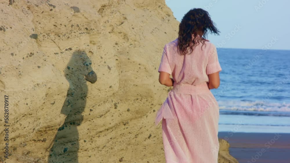 Woman on the sandy beach at sunset.
The brunette is undressing and getting ready to swim. The girl decided to sunbathe. Vacation and relaxation on the beach near the water.