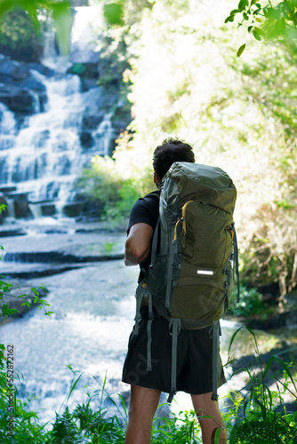 
young man walking with a travel backpack looks at the view towards the waterfalls in front of him