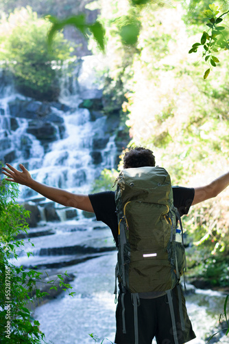 
young man walking with a travel backpack looks at the view towards the waterfalls in front of him