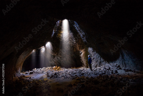 Adventurous athletic male standing in a lava tube looking at the sunlight shinning down into the cave through holes in the ceiling.
