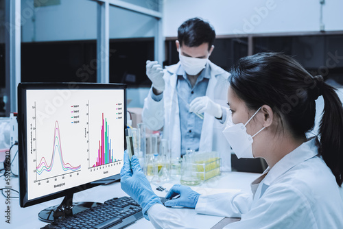 Scientist woman checked the analysis of UV, and nanoparticle size of the sample as shown on a monitor. Blurred background, scientist man experiment with the formulation of nanoparticles of the sample. photo