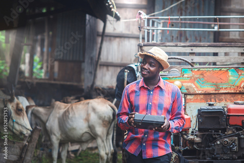 African farmer man listens retro radio broadcast receiver on shoulder stands happy smiling with old cow stall background
