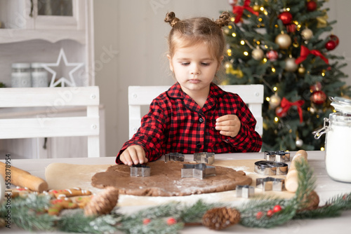 little girl in red pajama cooking festive gingerbread in christmas decorated kitchen