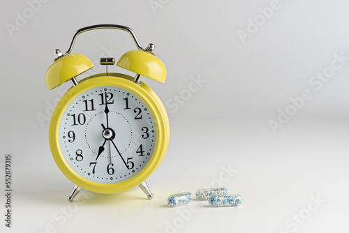 alarm clock on a light background with pills