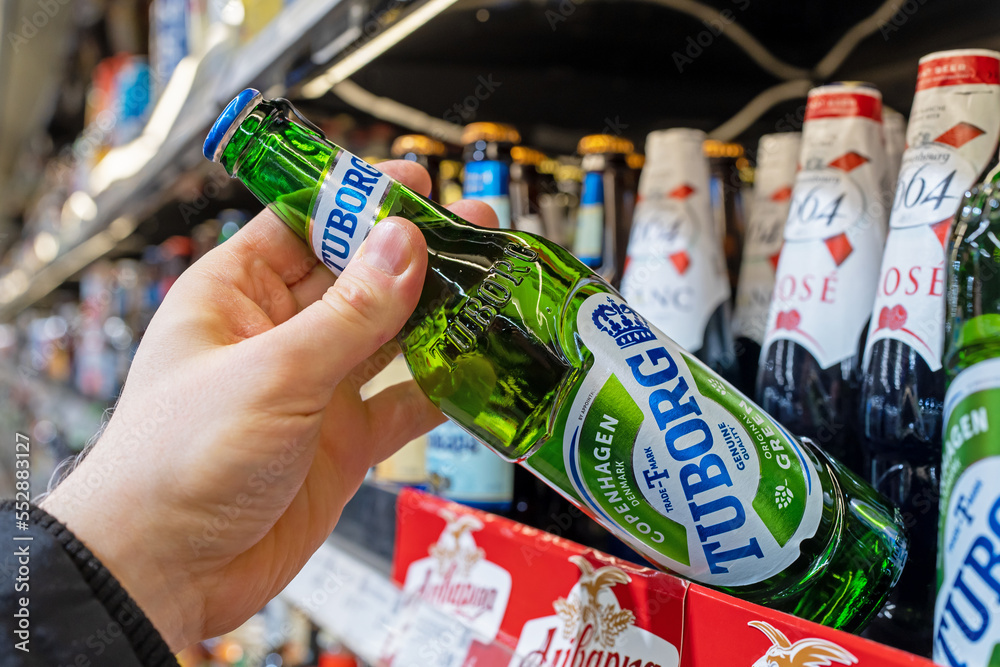 Stockfoto Tuborg beer bottles on shelves in a supermarket. Buyer takes  Tuborg beer. Hand is holding Tuborg beer. Minsk, Belarus, 2022 | Adobe Stock