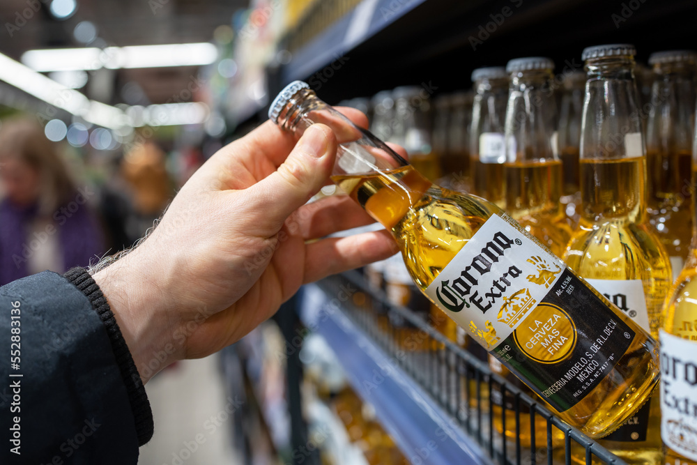 Corona extra beer bottles on shelves in a supermarket. Buyer takes Corona Extra beer. Corona