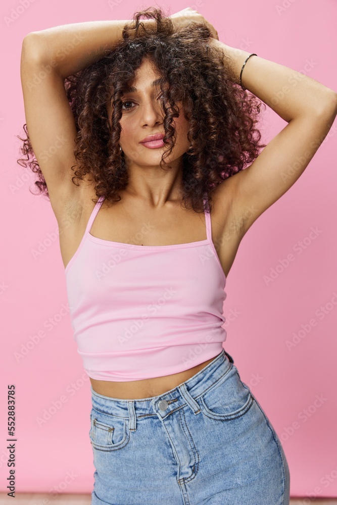 Woman with curly afro hair dancing in pink top and jeans on pink background, smile, copy place Woman with curly afro hair dancing in pink top and jeans on pink background, smile, copy place
