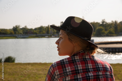 girl in a hat with wide brim and in a plaid shirt against the background of the river. selective focus