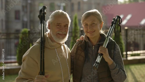 Portrait of the smiled mature family after scandinavian walking holding the trekking poles. Elderly couple before training standing outside. Aging youthfully photo