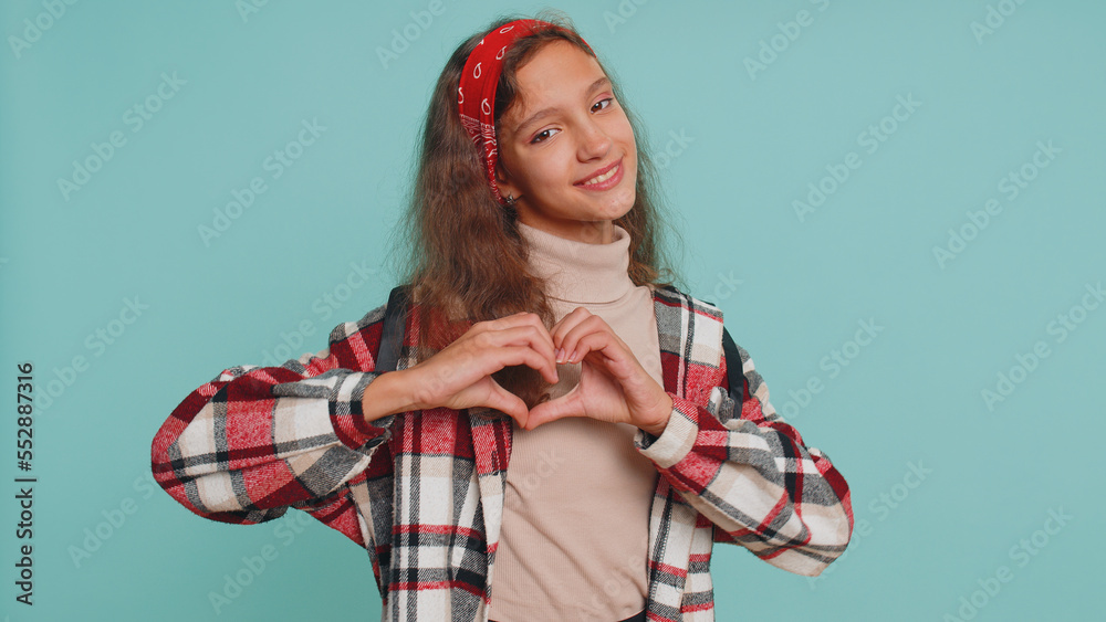 I love you. Smiling young teenager child girl kid makes heart gesture demonstrates love sign expresses good feelings and sympathy. Preteen children 12 years old isolated on studio blue wall background I love you. Smiling young teenager child girl kid makes heart gesture demonstrates love sign expresses good feelings and sympathy. Preteen children 12 years old isolated on studio blue wall background